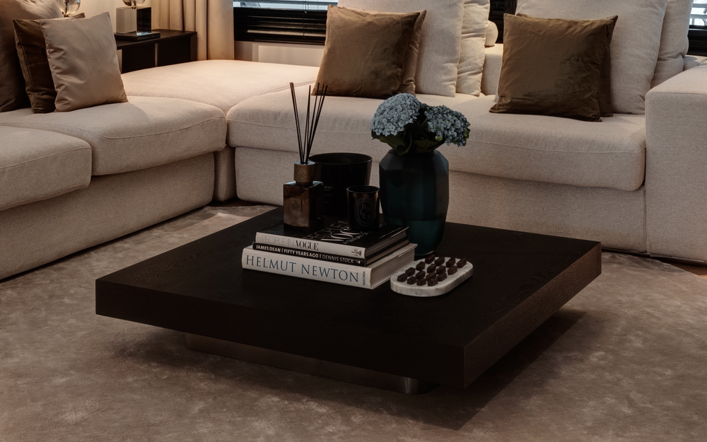 Lage salontafel Madison in Smoke Wood met boeken en bloemen voor een lichte hoekbank.