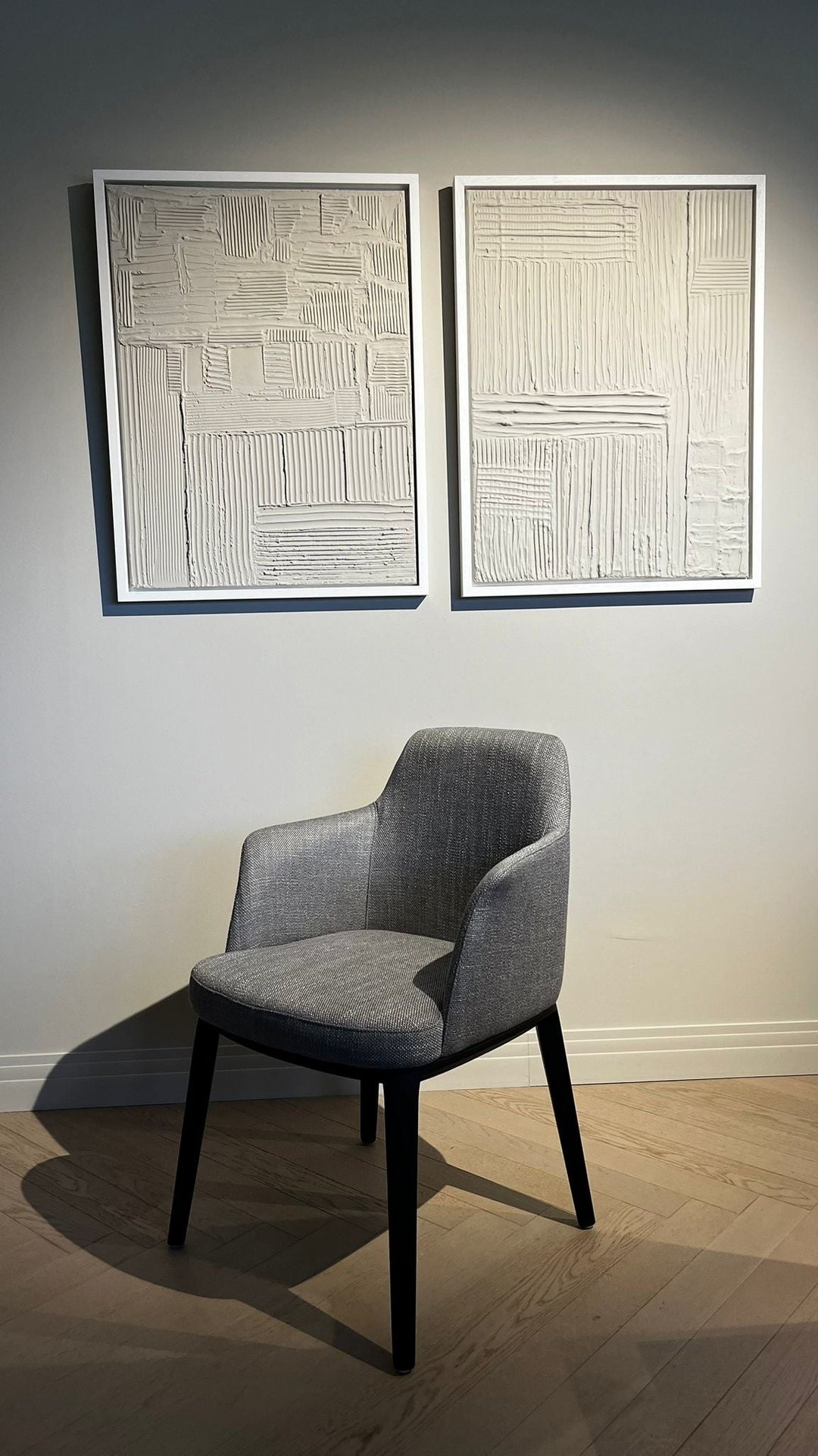 Eetkamerstoel Milano in grijs met zwarte houten poten op een houten vloer onder twee wandkunstwerken.