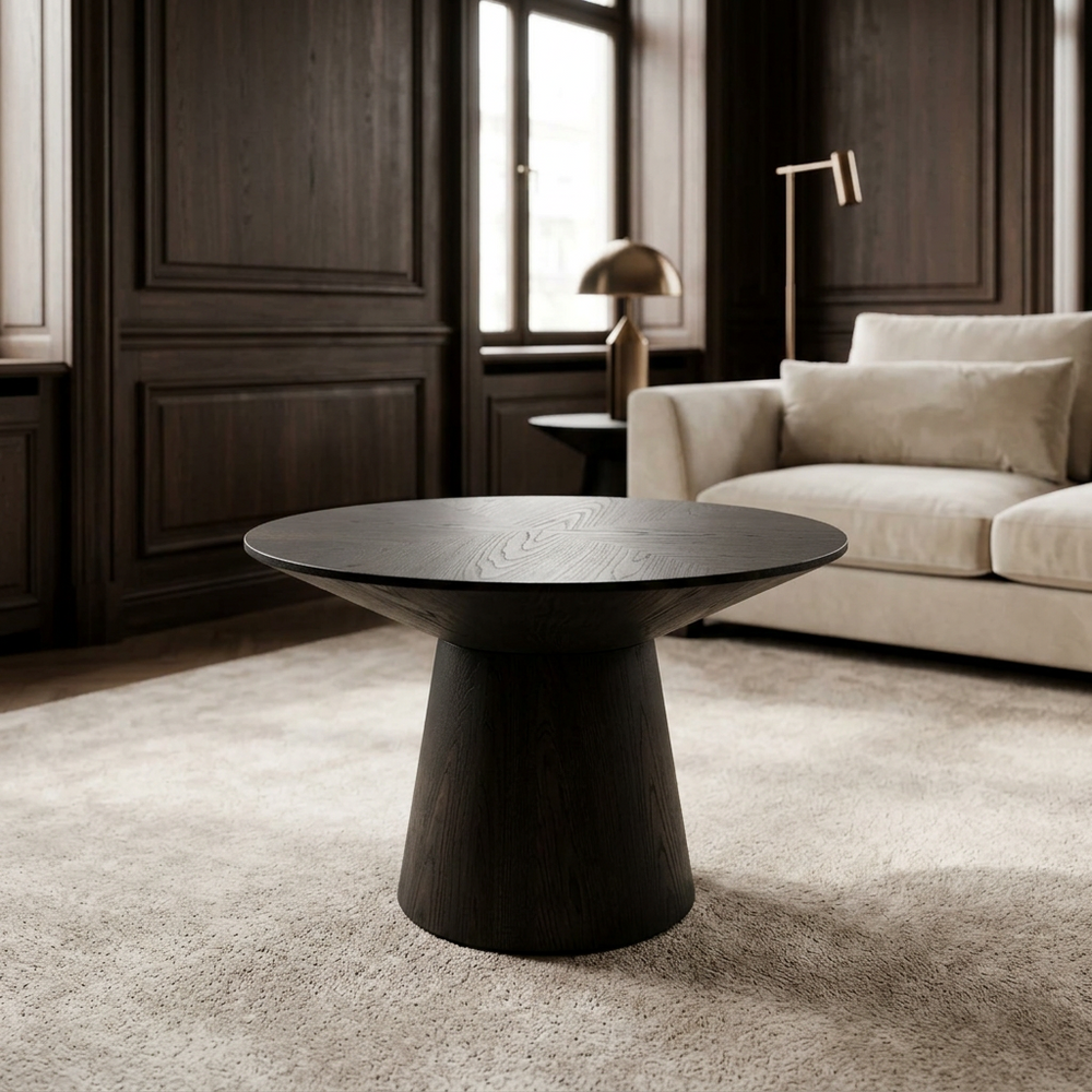 Ronde bijzettafel Amalfi in zwart geolied eiken bij een crème bank en donkerhouten wandpanelen.